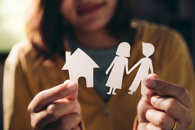 Foto manos de mujer sosteniendo pareja de papel y casita en concepto de relación de sala, familia y personas.