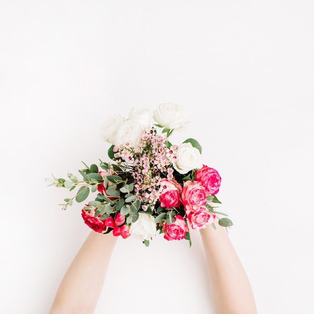 Manos de mujer sosteniendo ramo de novia con rosas blancas, rosadas y rojas, rama de eucalipto, flores silvestres sobre fondo blanco. Endecha plana, vista superior