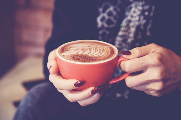 Manos de mujer sosteniendo rojo taza de café con leche