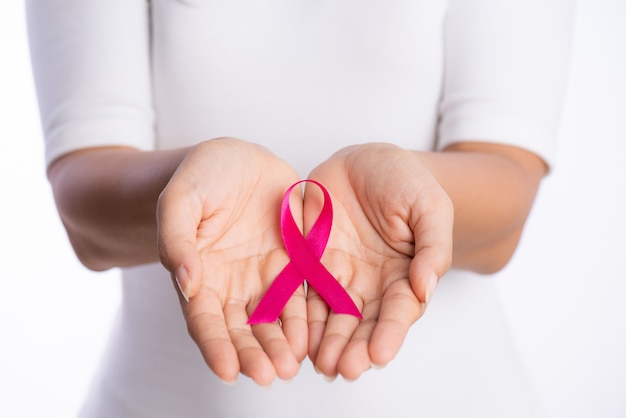 Manos de mujer sosteniendo rosa cinta de conciencia de cáncer de mama en blanco