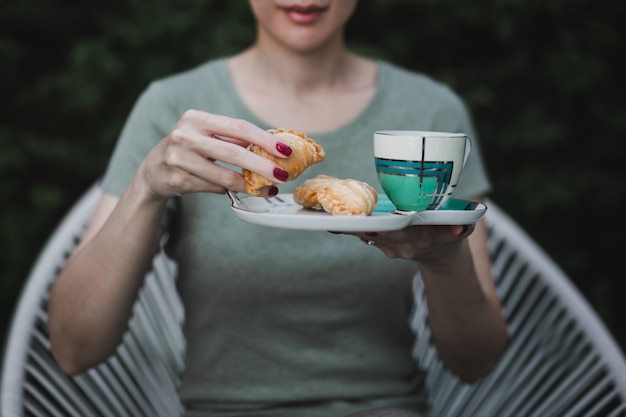 Manos de mujer sosteniendo snack con taza de café sentado en el jardín en casa.