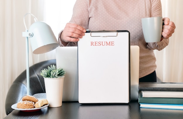 Manos de mujer sosteniendo la solicitud de currículum cerca de su lugar de trabajo con computadora portátil.