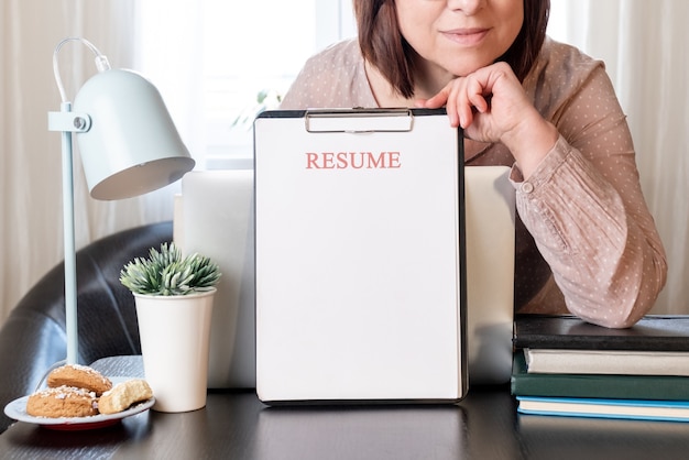 Manos de mujer sosteniendo la solicitud de currículum cerca de su lugar de trabajo con computadora portátil.