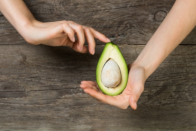 Manos de mujer sosteniendo suavemente medio corte de aguacate contra la mesa de madera