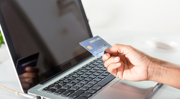 Manos de mujer sosteniendo una tarjeta de crédito y usando una computadora portátil con la compra del producto en casa
