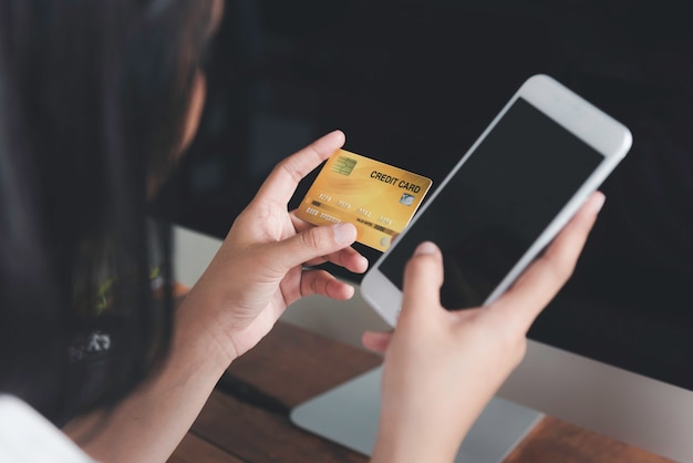 Manos de mujer sosteniendo una tarjeta de crédito y usando un teléfono inteligente para compras en línea o comercio electrónico