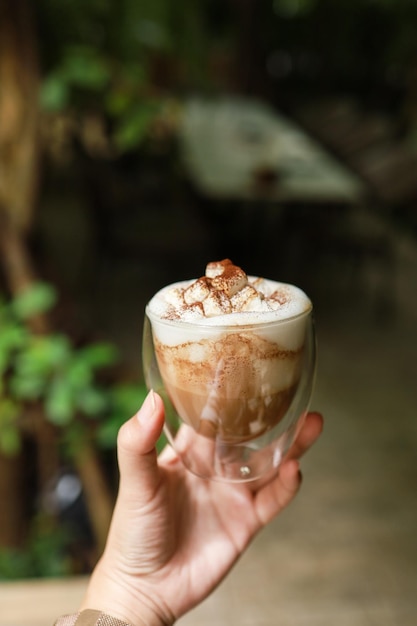 Manos de mujer sosteniendo una taza de café con arte latte sosteniendo una taza de té o café en la mañana