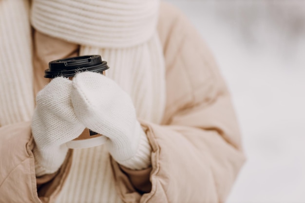 Las manos de la mujer sosteniendo una taza de café caliente y disfrutando del clima invernal en la calle nevada