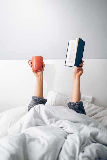 Manos de mujer sosteniendo una taza de café y un libro por la mañana al despertar