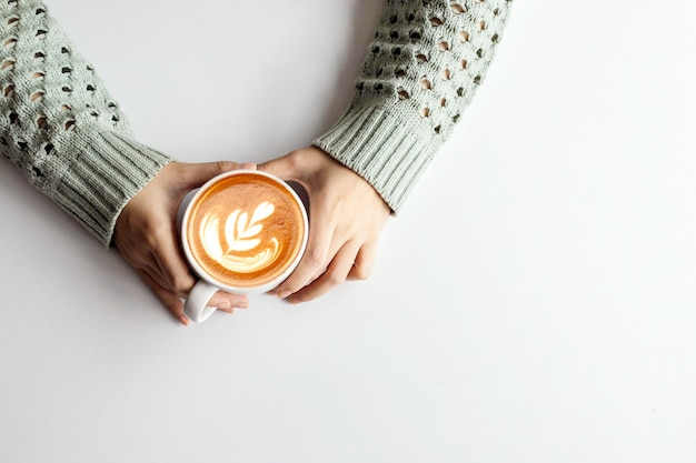 Manos de mujer sosteniendo una taza con café en la vista superior del fondo de la mesa blanca