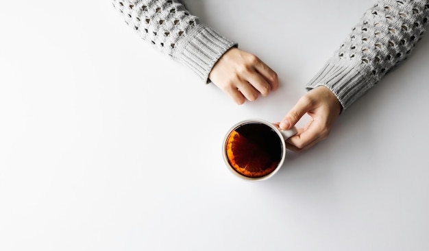 Manos de mujer sosteniendo una taza con café en la vista superior del fondo de la mesa blanca