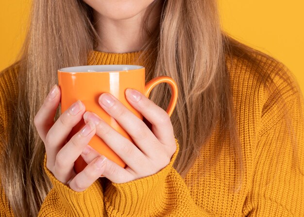 Manos de mujer sosteniendo una taza sobre fondo amarillo