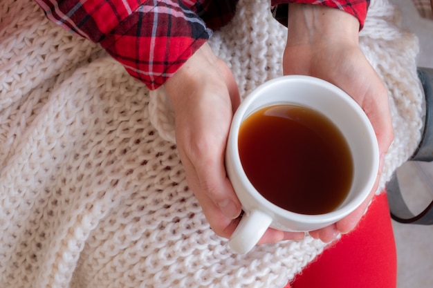 Foto manos de mujer sosteniendo tazas de té o café vestidas con ropas festivas rojas y blancas.