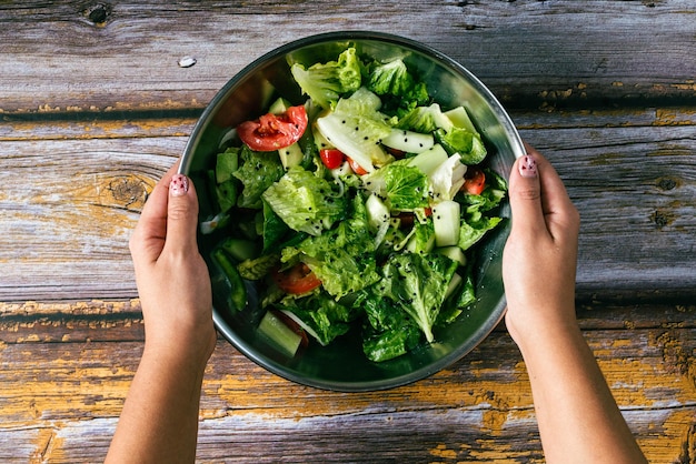 Manos de mujer sosteniendo un tazón con ensalada en la mesa de madera Comida saludable