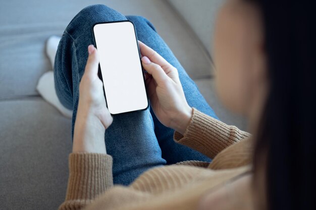 Manos de mujer sosteniendo un teléfono inteligente con pantalla en blanco blanco maqueta pantalla vacía para anuncios de aplicaciones de redes sociales en casa