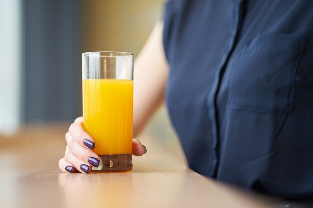 Manos de mujer sosteniendo un vaso de jugo de naranja