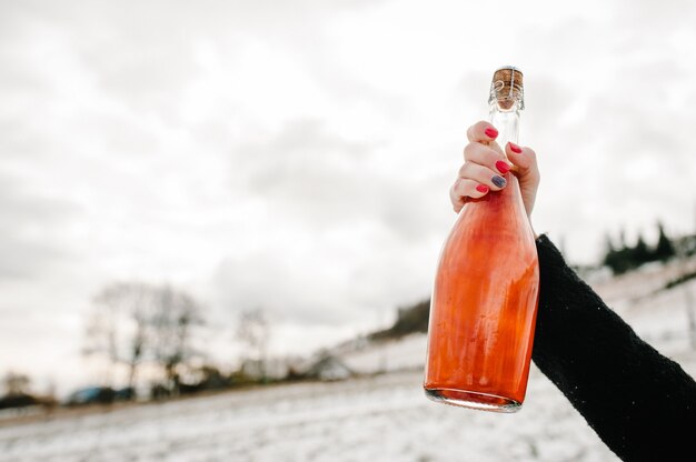 Las manos de la mujer sostienen una botella de champán contra las montañas de invierno.