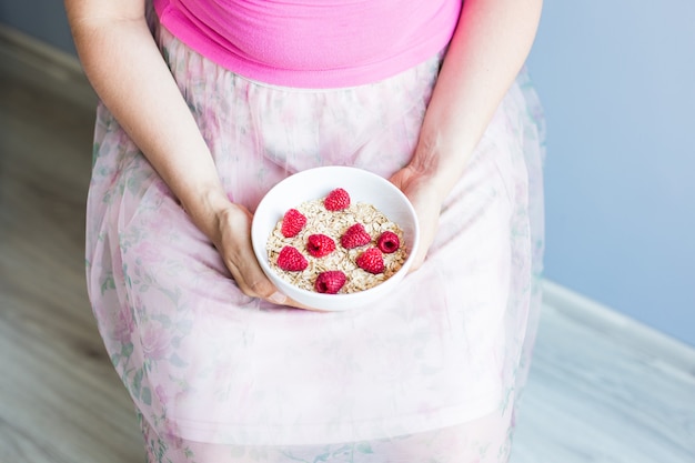 Las manos de la mujer sostienen un desayuno saludable y natural, avena y frambuesas en un bol.