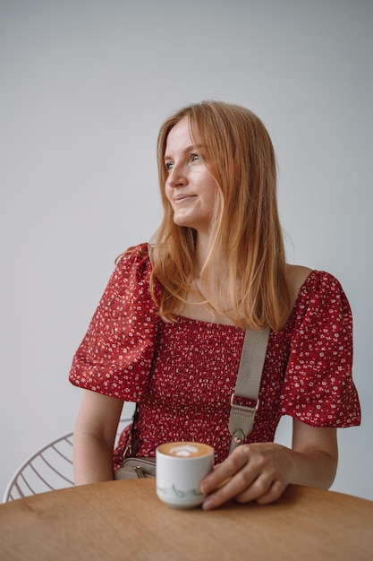 Manos de mujer sostienen una hermosa taza de capuchino aromático o café con leche en una mesa de madera en un acogedor café