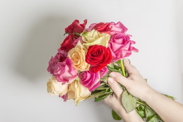 Las manos de la mujer sostienen un hermoso ramo de rosas multicolores frescas