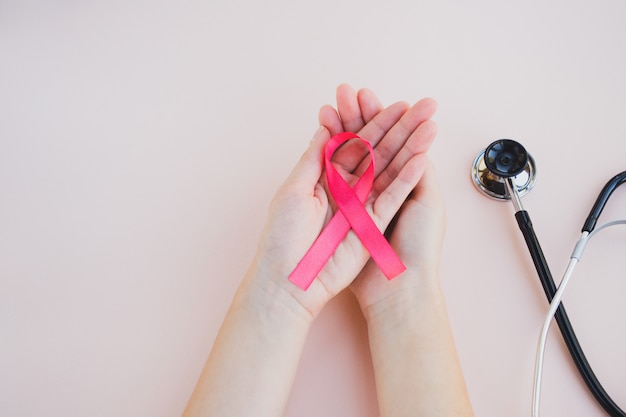 Las manos de la mujer sostienen el símbolo de cinta de conciencia de cáncer de mama rosa