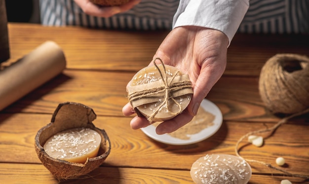 Manos de mujer sostienen un trozo de jabón de coco blanco hecho a mano y coco fresco Concepto de hacer y usar jabón natural y cosméticos ecológicos un pasatiempo creativo interesante