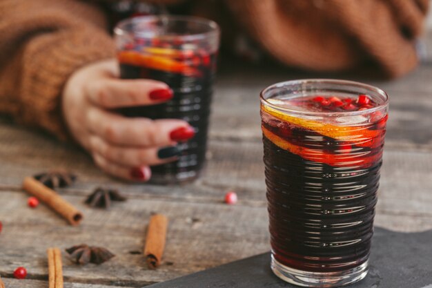 Manos de mujer en suéter caliente sosteniendo una copa de vino caliente