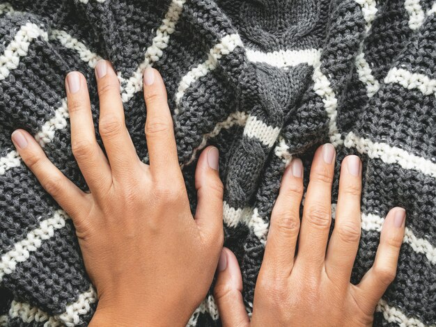 Manos de mujer en suéter de punto gris con rayas blancas. Ropa abrigada doblada.