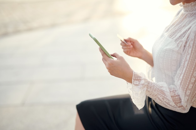 Manos de mujer con tarjeta de crédito y uso de teléfono celular para compras en línea al aire libre