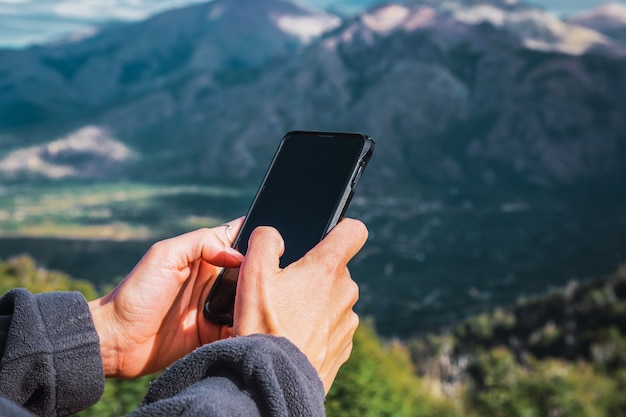 Manos de mujer con teléfono celular entre las montañas.