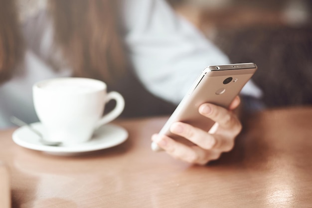 Manos de mujer con teléfono inteligente, auriculares y taza de té. Para montaje de pantalla gráfica