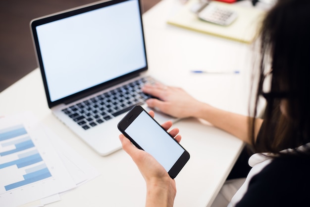 Manos de mujer con teléfono móvil y computadora portátil en la oficina