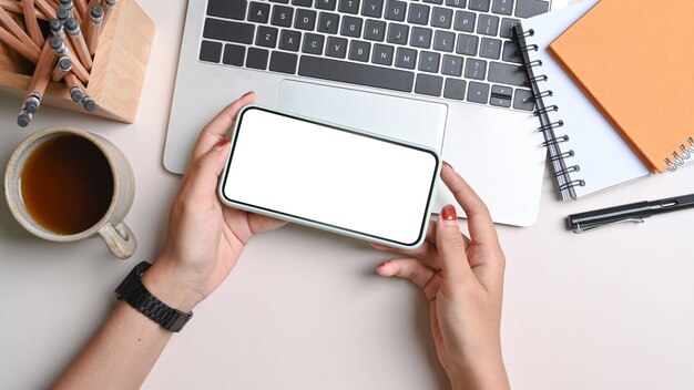 Manos de mujer con teléfono móvil horizontal sobre escritorio blanco.