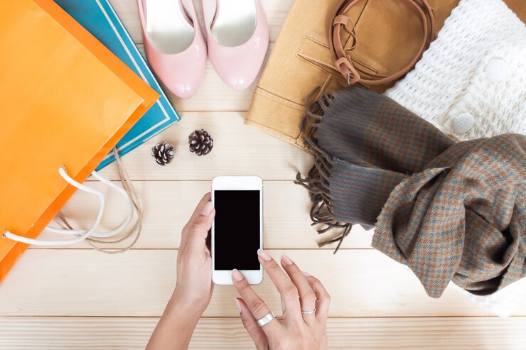 Foto manos de mujer con teléfono móvil con ropa y accesorios, vista superior, compras de otoño