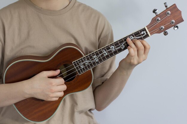 Manos de mujer tocando el ukelele en el fondo gris