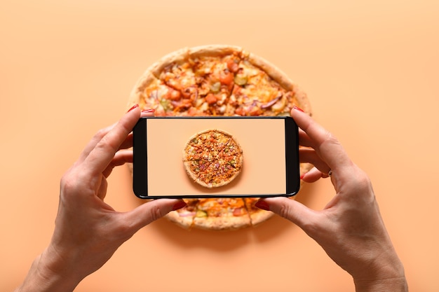 Foto manos de mujer toma fotografía de pizza vegana italiana con tomate, mozzarella, salsa