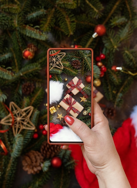 Manos de mujer tomando una foto móvil de la vista superior de la composición navideña
