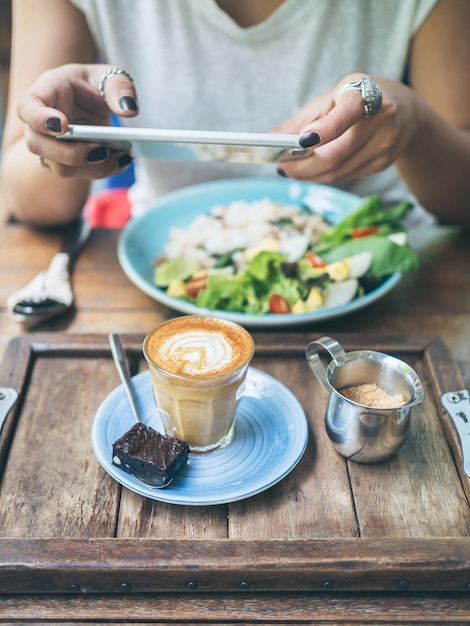 Manos de mujer tomando fotos de una taza de café en una mesa de madera con un teléfono inteligente