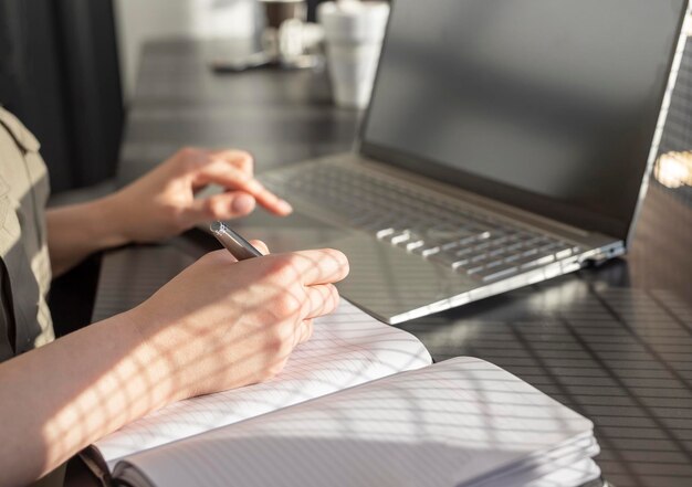 Manos de mujer tomando notas en el planificador y trabajando en una computadora portátil en un café concepto de educación y trabajo en línea