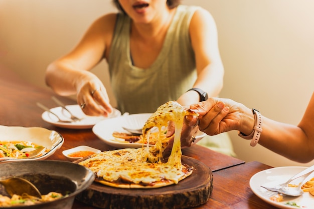 Manos de mujer tomando porciones de pizza con amigos