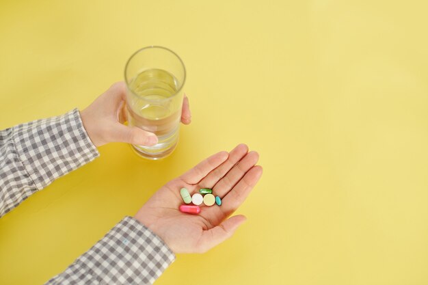 Manos de mujer tomando un puñado de pastillas y tabletas de colores y un vaso de agua, vista desde arriba