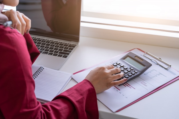 Manos de mujer trabajando con calculadora sobre planificación financiera personal en café.