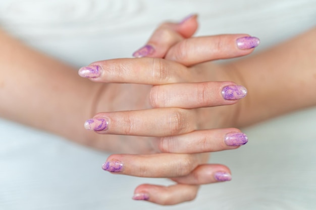 Las manos de una mujer con uñas moradas y esmalte de uñas morado.