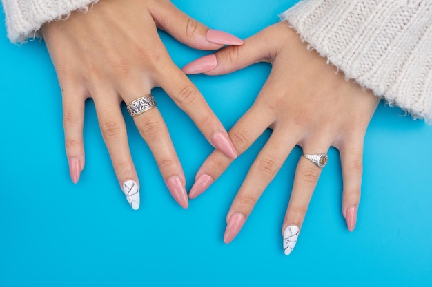 manos de mujer con uñas rosas esculpidas con anillos y un fondo azul claro