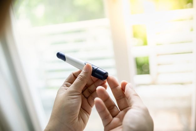 Foto manos de mujer usando lanceta en el dedo para controlar el nivel de azúcar en la sangre de la diabetes por el medidor de glucosa en la mañana