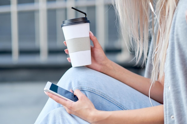 Manos de mujer usando teléfono y sosteniendo taza de papel con café