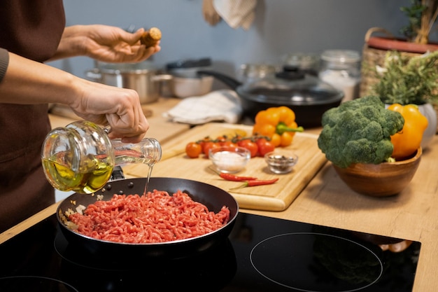 Manos de mujer vertiendo aceite de oliva en una sartén con carne picada cruda