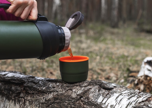 Manos de mujer vertiendo té del termo en una taza en el descanso de la bebida caliente de fondo de la naturaleza durante el campamento