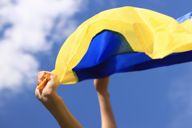 Manos de mujeres con la bandera ucraniana contra el cielo La bandera ucraniana ondea en el viento