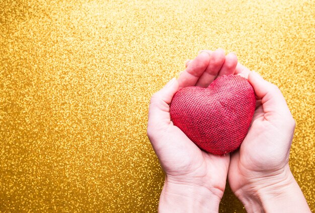 Manos de mujeres con corazón rojo sobre brillo